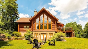 Une cabane en rondins dotée d’une grande véranda à l’avant, d’une terrasse et d’une pelouse bien entretenue.