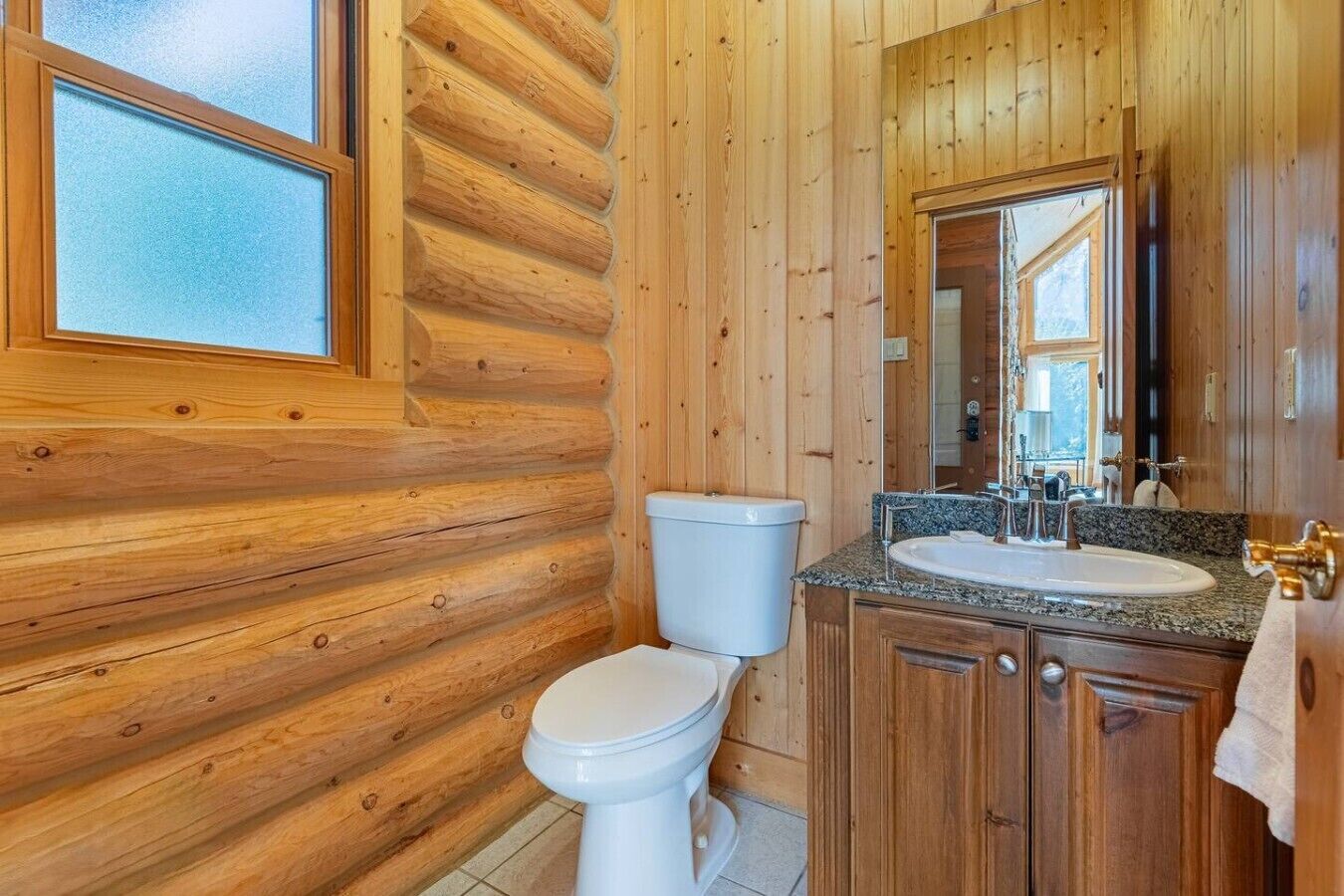 Un baño de cabaña de madera con inodoro, lavamanos y espejo.