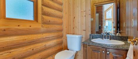 Un baño de cabaña de madera con inodoro, lavamanos y espejo.