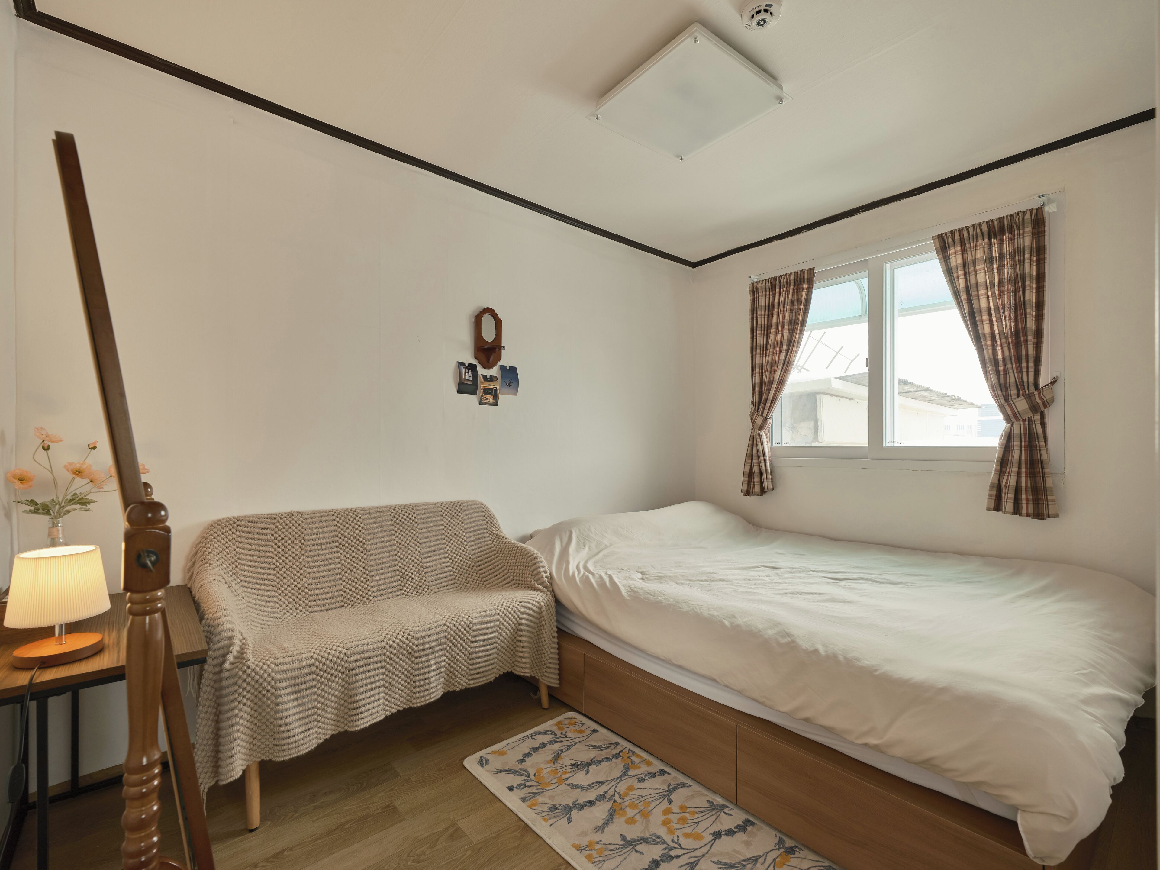 Una camera da letto con un letto, un tavolino con una lampada, una sedia, una finestra con tende e una sveglia a muro.