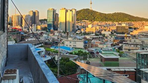 Un paisaje urbano con edificios altos, una torre destacada y un fondo montañoso.