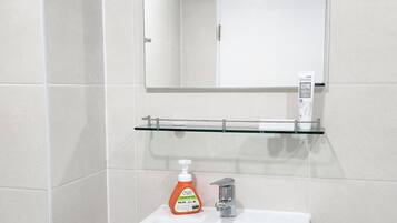 Een badkamer met een wit wastafelmeubel, een spiegel erboven en een glazen plankje met een flesje handdesinfecterend middel.