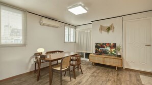 Un comedor con una mesa y sillas de madera, un televisor sobre un mueble de madera, y una ventana con persianas.