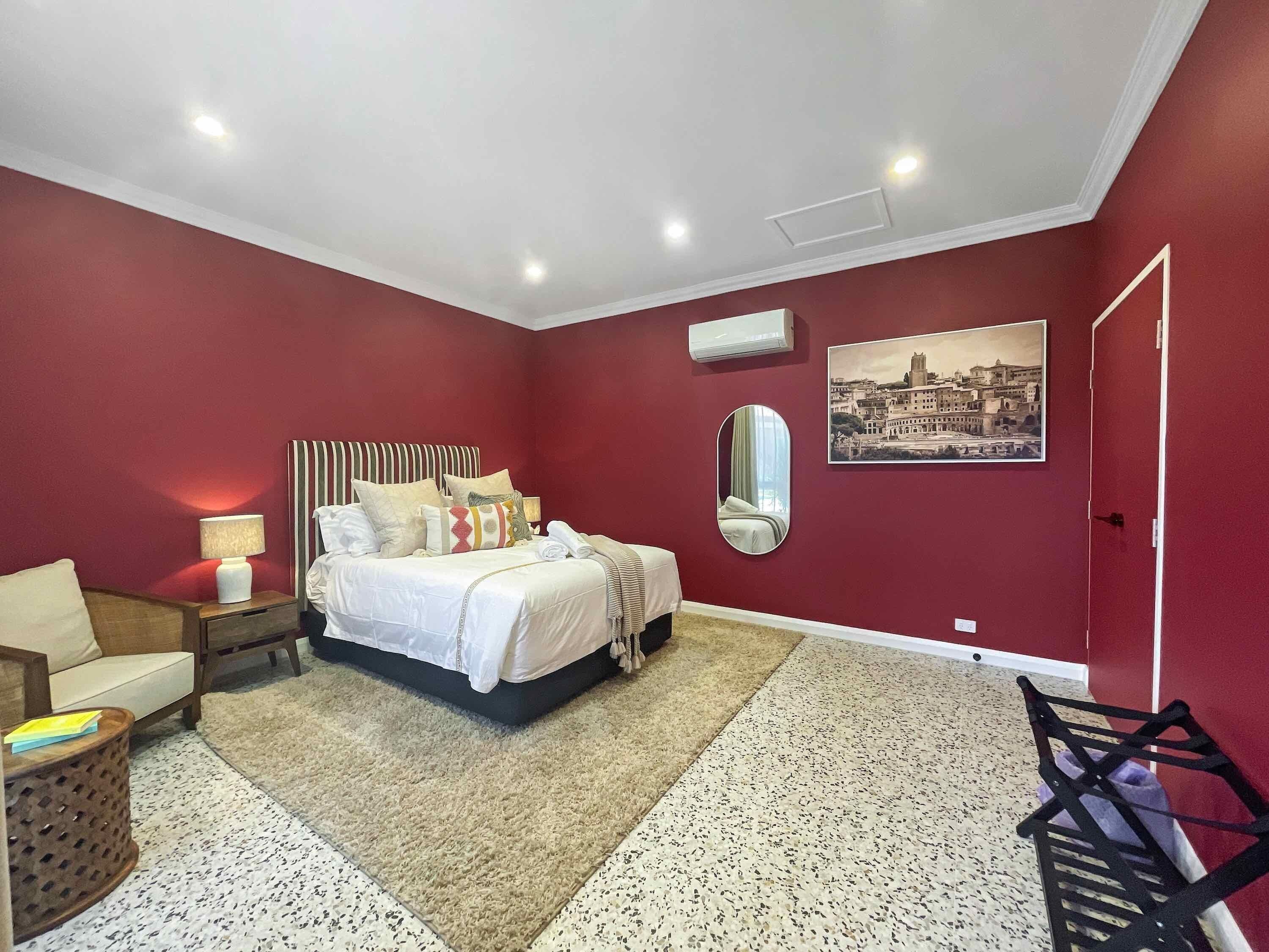 Une chambre à coucher avec un lit, une table de chevet, une chaise, un miroir et un tableau accroché au mur.