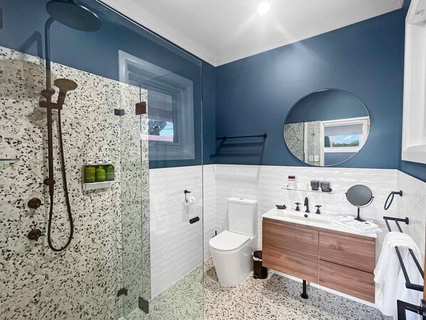 Een moderne badkamer met een douchecabine van glas, wandtegels in wit en blauw, een houten wastafelmeubel en een ronde spiegel.