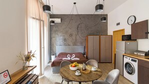 Une chambre d’hôtel moderne équipée d’un lit, d’une table à manger avec des chaises, d’un lave-linge et d’une kitchenette.