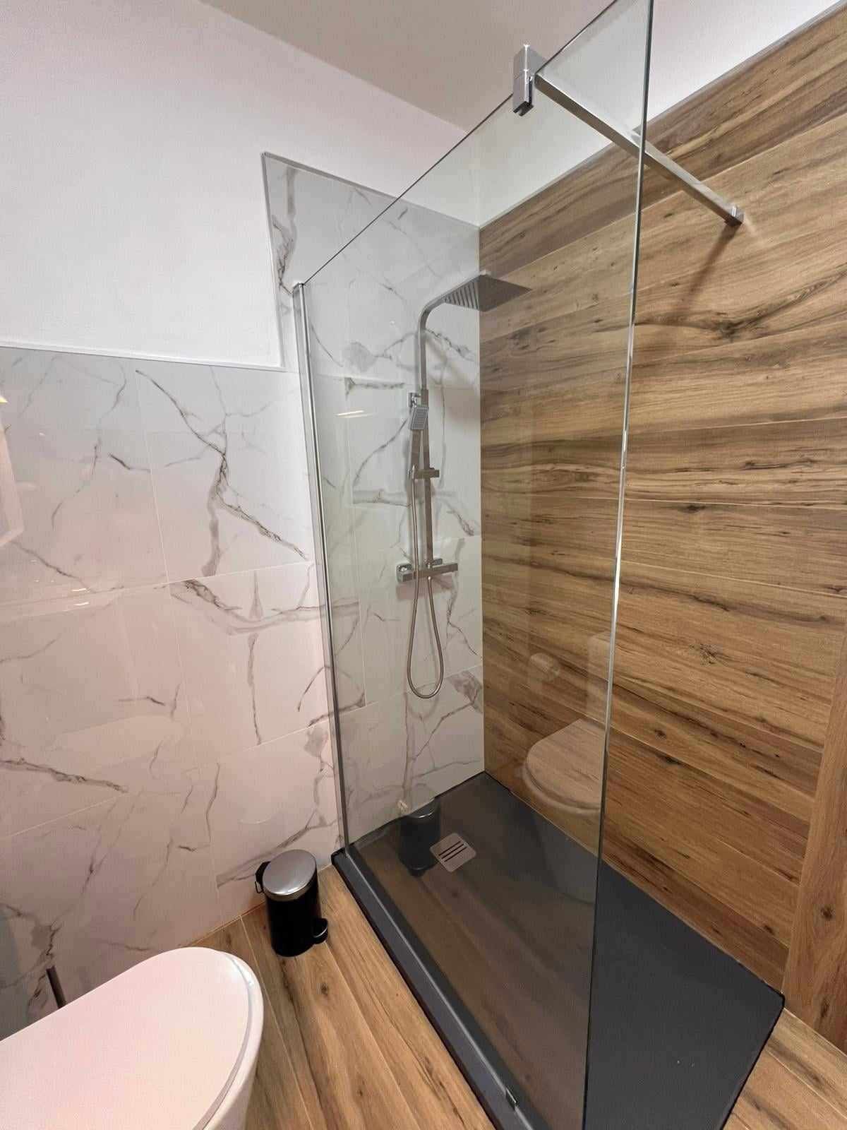 Ett modernt badrum med en duschavdelning med glasväggar, väggar i marmor och trädetaljer.