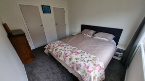 A bedroom with a bed, a nightstand, a dresser, and a door. - Tidy Three Bedroom Home in Ruakaka. (Ruakākā)