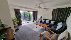 A living room with a sofa, a coffee table, and a chair. There is a sliding glass door leading to a balcony. - Tidy Three Bedroom Home in Ruakaka. (Ruakākā)