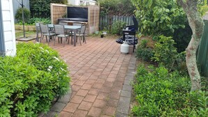A patio with a grill, table, and chairs. - Tidy Three Bedroom Home in Ruakaka. (Ruakākā)