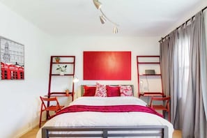 Una camera da letto ordinata con un letto, due comodini, una parete rossa a contrasto e una finestra con tende.