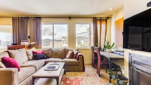 A living room with a sofa, coffee table, and TV. There are windows with curtains, a fireplace, and a dining area with chairs and a table. - Two  Bedroom, Two Newly Renovated Bathrooms, Deck (San Francisco)