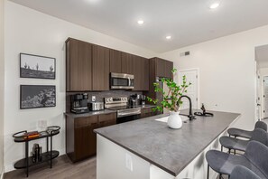 A modern kitchen with dark wood cabinets, stainless steel appliances, a central island with bar stools, and a potted plant.