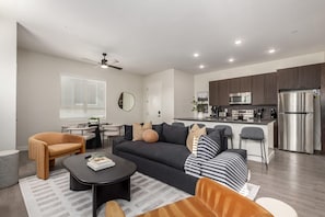 A modern living room with a sofa, coffee table, and chairs, a dining area with a table and chairs, and a kitchen with appliances. - Macallister Luxe 1006 | Desert Views & Heated Pool (Scottsdale)