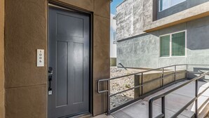 Une entrée moderne avec une porte sombre, une rampe d’appui en métal et une façade en béton.