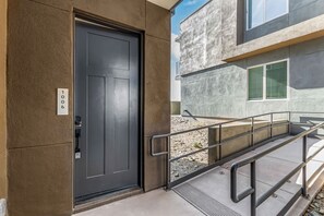 Une entrée moderne avec une porte sombre, une rampe d’appui en métal et une façade en béton.