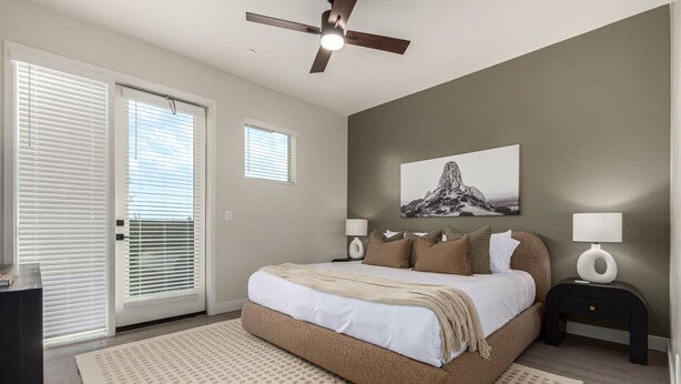 A bedroom with a bed, two bedside tables with lamps, a ceiling fan, a large window with blinds, and a wall-mounted artwork. - The Macallister | Luxe 2BR Near TPC Scottsdale (Scottsdale)
