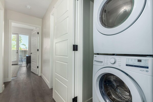A laundry room with stacked front-loading washers and dryers, a hallway with white doors, and a view of the outside through a door. - Macallister 1007|N Scottsdale|Close2Golf|Htd Pool (Scottsdale)