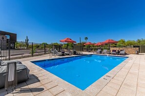 A swimming pool with lounge chairs and red umbrellas, surrounded by a stone wall and a metal fence. - Macallister Luxe 1008 | Close to Golf |Heated Pool (Scottsdale)