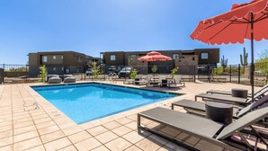 A swimming pool with lounge chairs and umbrellas, surrounded by a fenced patio area with modern buildings in the background. - Macallister Luxe 1008 | Close to Golf |Heated Pool (Scottsdale)