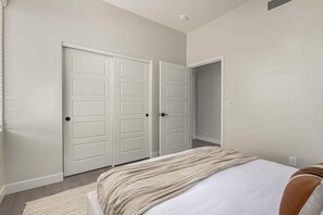 A bedroom with two white wardrobes, a bed with a beige blanket, and a light-colored carpet. - Macallister Luxe 1008 | Close to Golf |Heated Pool (Scottsdale)