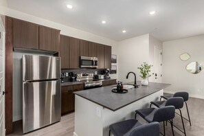 A modern kitchen with stainless steel appliances, a central island with bar stools, and a minimalist design. - Macallister Luxe 1008 | Close to Golf |Heated Pool (Scottsdale)