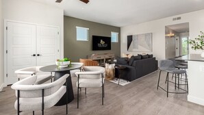 Ein modernes Wohnzimmer mit einem runden Tisch, grauen Sesseln, einer Couch, einem Fernseher und einem Deckenventilator.