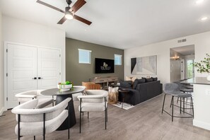 Un salon moderne avec une table ronde, des fauteuils gris, un canapé, un téléviseur et un ventilateur de plafond.