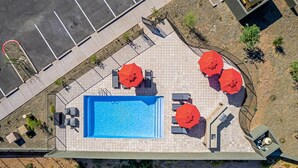 Eine Vogelperspektive auf einen Poolbereich mit einem rechteckigen Pool, umgeben von Fliesenböden und vier roten Sonnenschirmen.