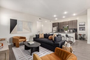 A modern living room with a sofa, coffee table, and chairs, a kitchen with appliances, and a dining area.