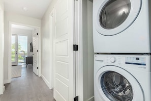 A laundry room with stacked washers and dryers, a hallway leading to a door, and a view of a balcony with blinds. - Macallister 2008|Heated Pool|Close 2 Golf|BBQ|View (Scottsdale)