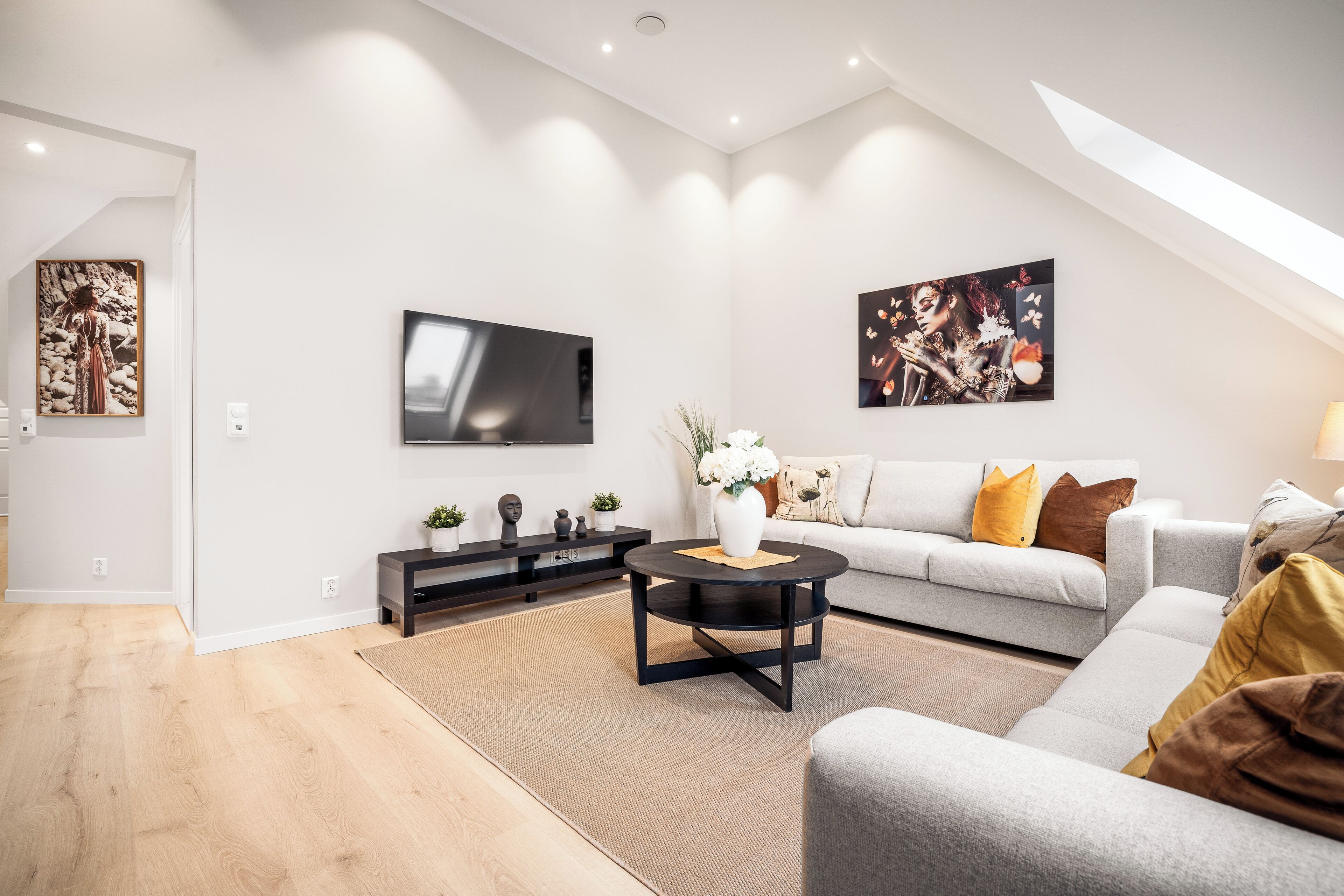 Ein modernes Wohnzimmer mit Flachbildfernseher, einer Couch, einem Couchtisch und Kunstwerken an den Wänden.