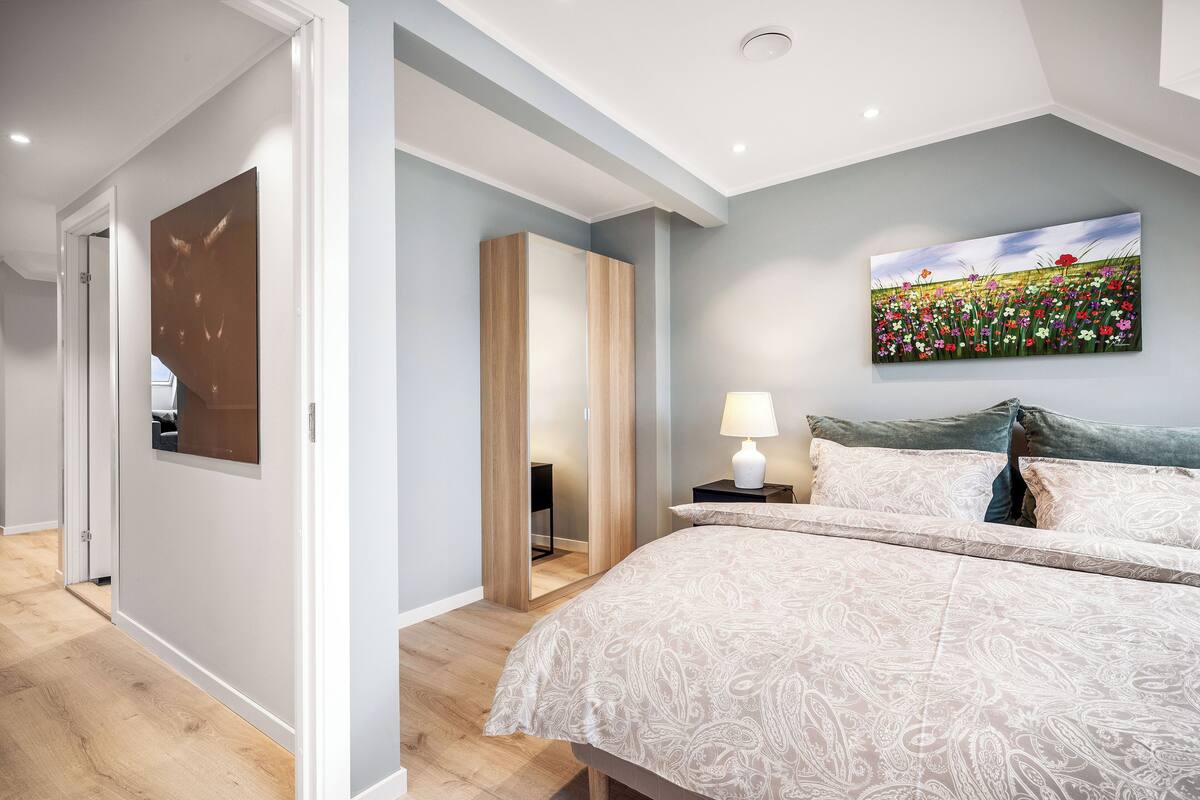A bedroom with a large bed, a nightstand, a painting, and a wardrobe.