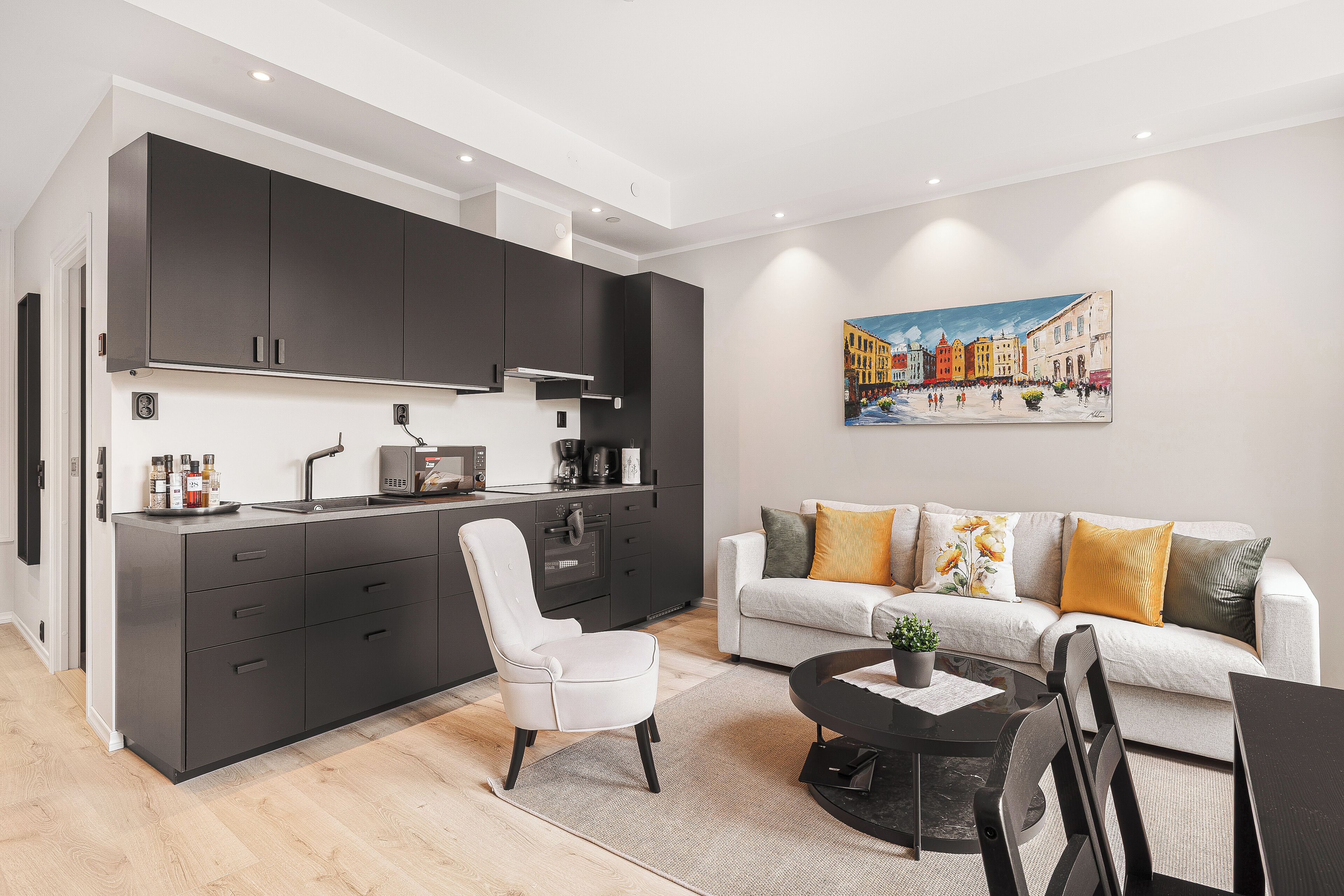 A modern kitchen with dark cabinets, a white chair, and a dining area with a table and chairs.