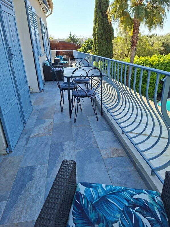 A patio with a table and chairs, a wicker bench, and a railing.