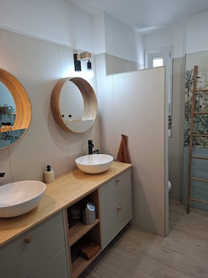 Ein modernes Badezimmer mit einem Holzlagerfeld, zwei runden Spiegeln, einem weißen Waschbecken und einem Handtuchhalter.