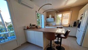 A modern kitchen with a central island, bar stools, and a view of the outside.