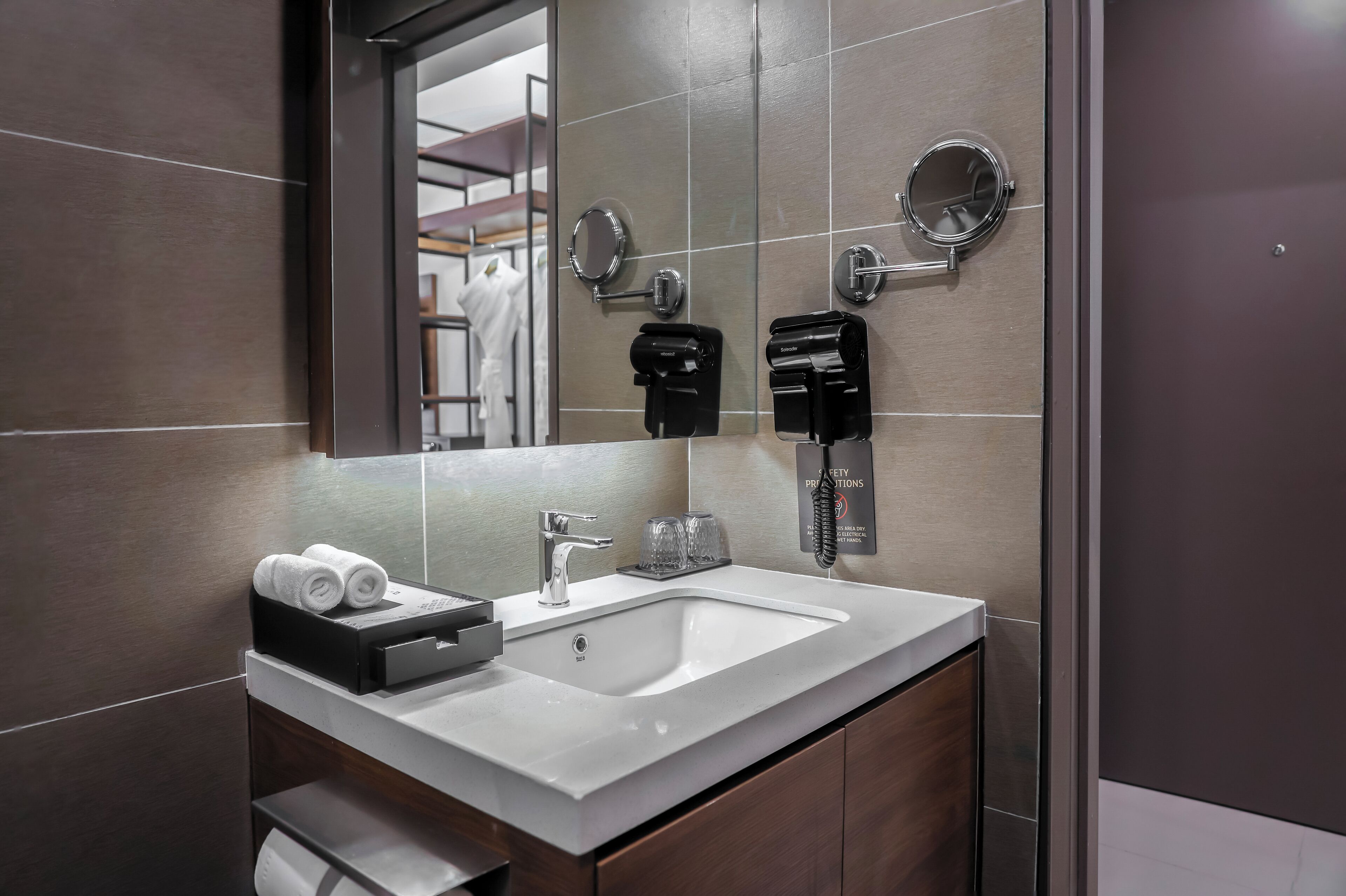 Un bagno moderno con un lavandino bianco, due specchi, un dispenser di asciugamani e un dispenser di sapone in vetro.