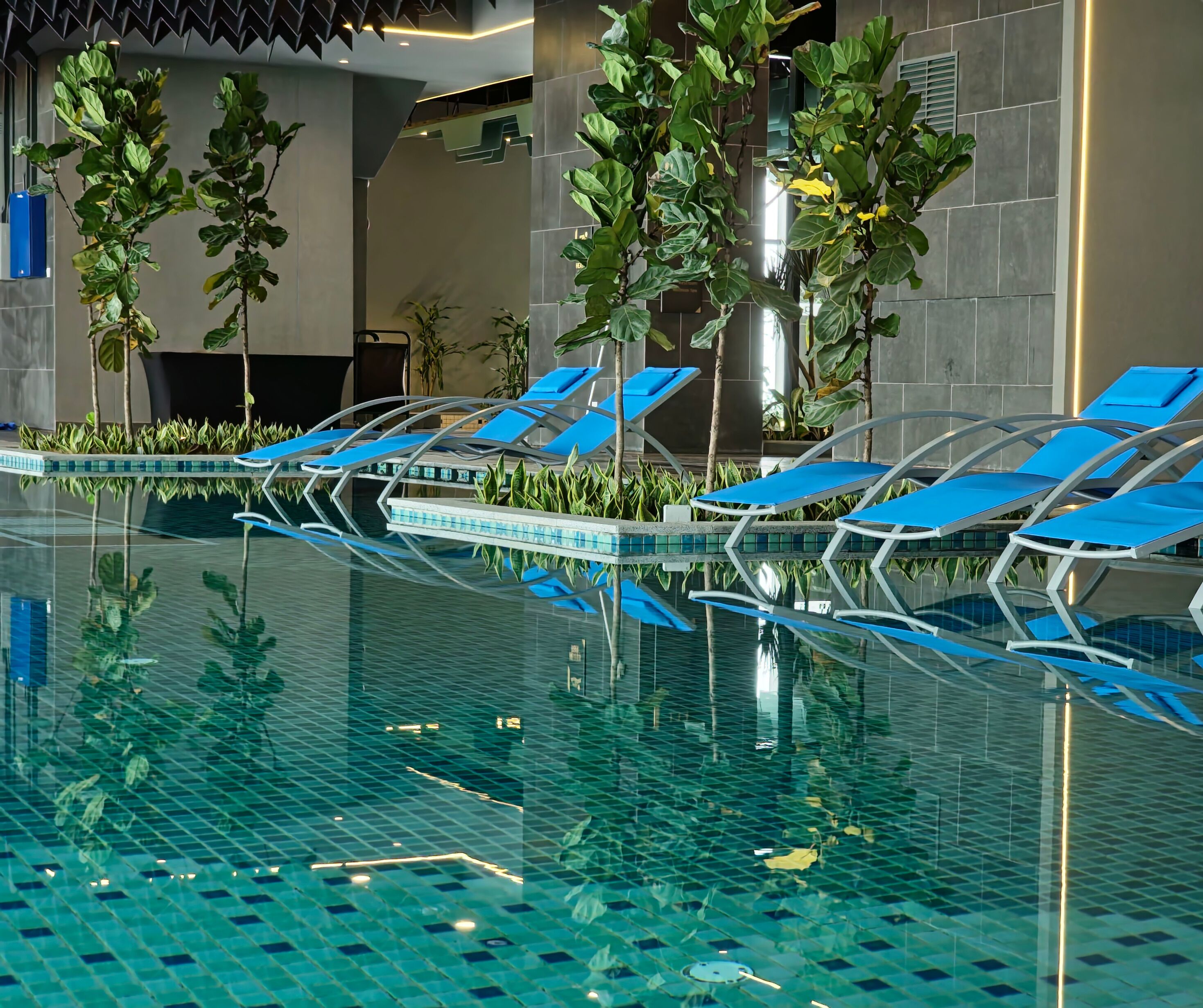 An indoor swimming pool with blue lounge chairs and potted plants.