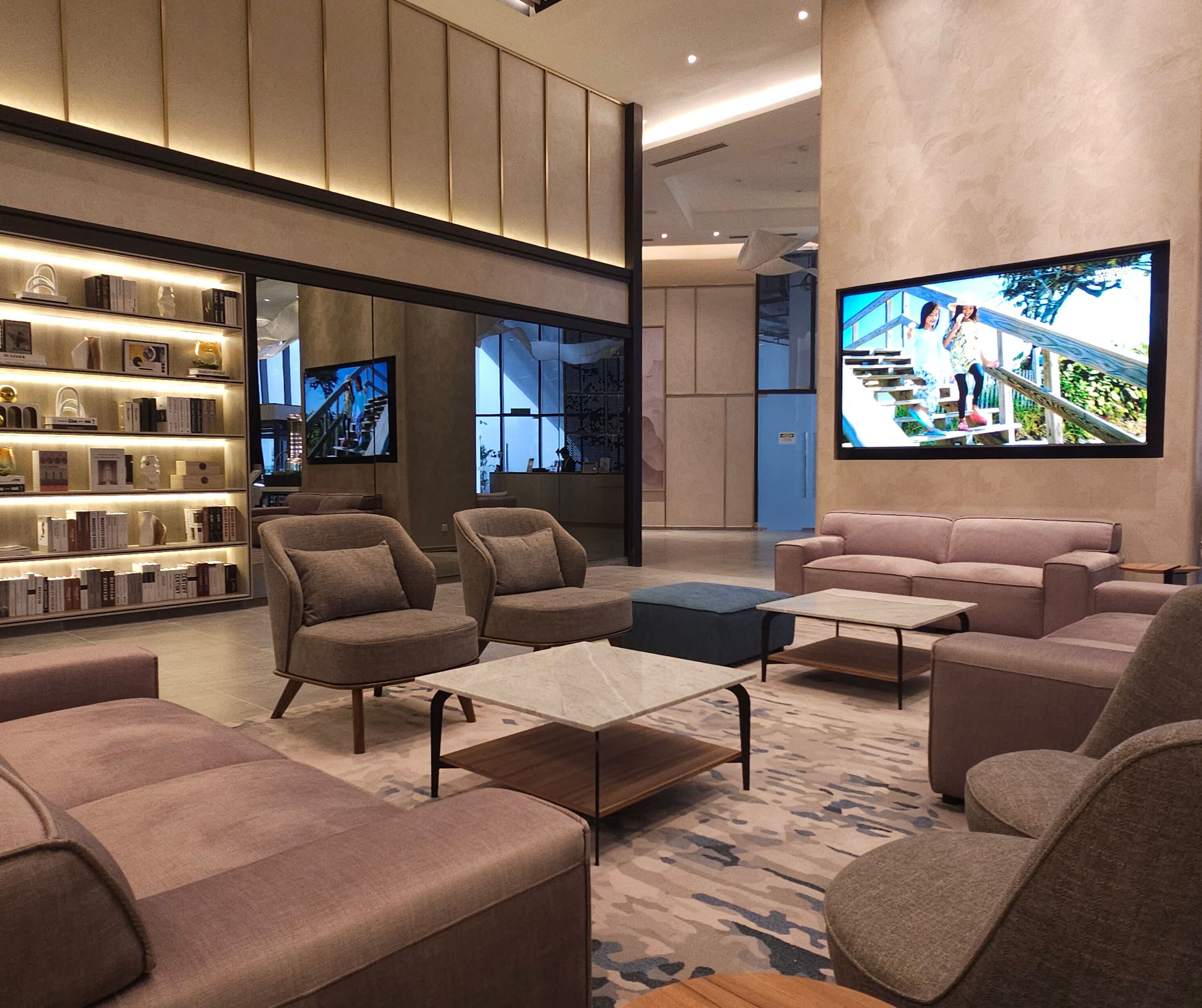 A modern lobby with sofas, a coffee table, a bookshelf, and a TV displaying a cityscape.