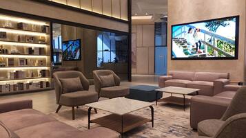 A modern lobby with sofas, a coffee table, a bookshelf, and a TV displaying a cityscape.