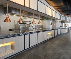 A modern kitchen with a long counter, copper pendant lights, and stainless steel appliances.