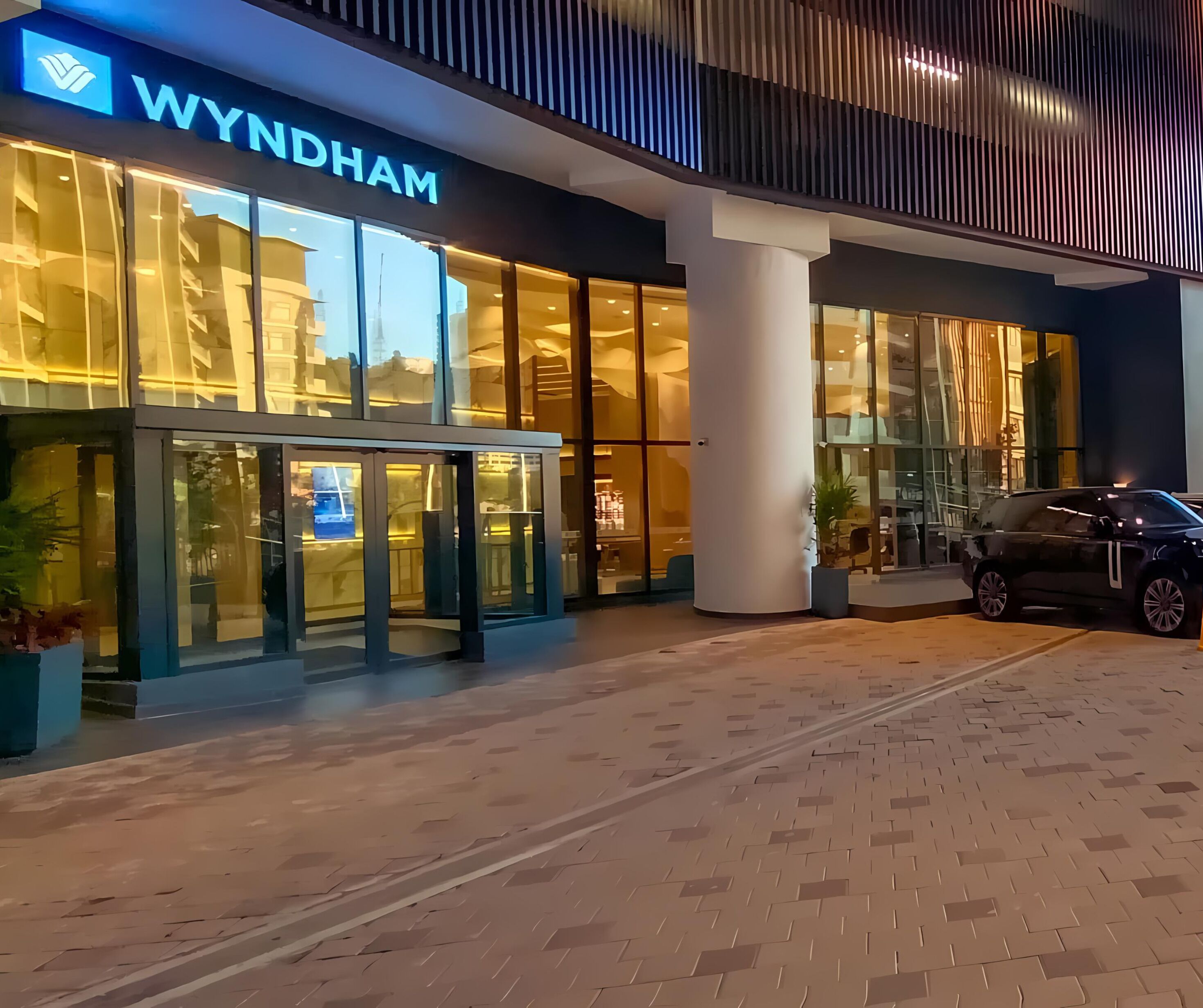 A Wyndham hotel entrance with a glass facade, a central column, and a car parked outside.