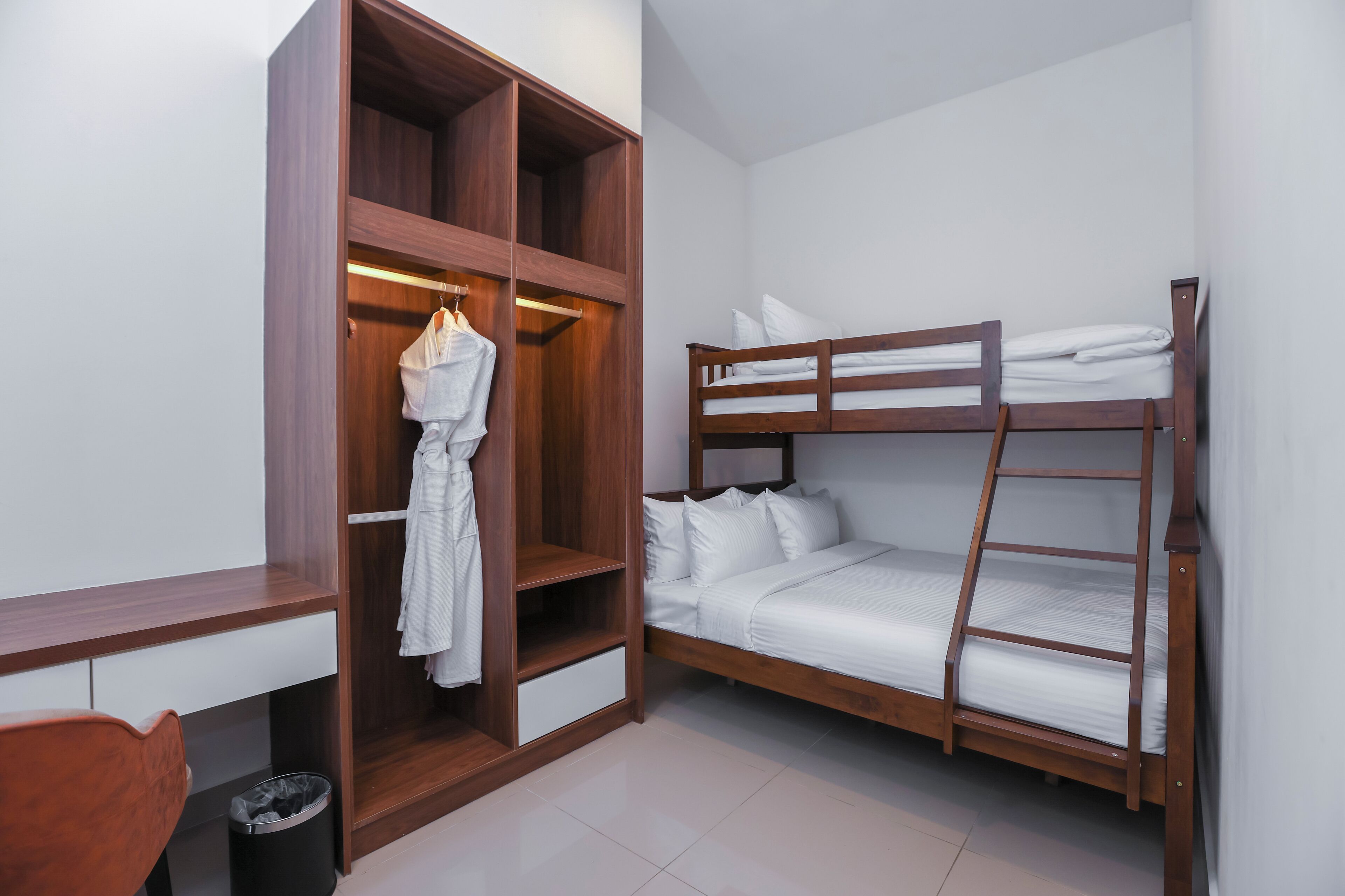 A room with a bunk bed, wooden wardrobe, and a desk with a chair.