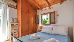 Un dormitorio con cama, un armario de madera, una mesita de noche con lámpara y una ventana con vistas a zonas verdes.