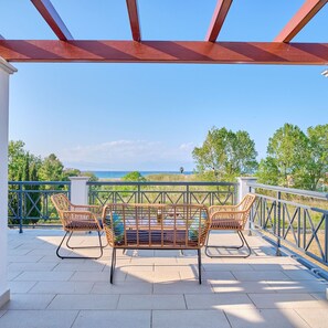 A covered outdoor seating area with wicker furniture and a view of the sea. - Utopia Beach Villa in Ionian Islands (Corfu)