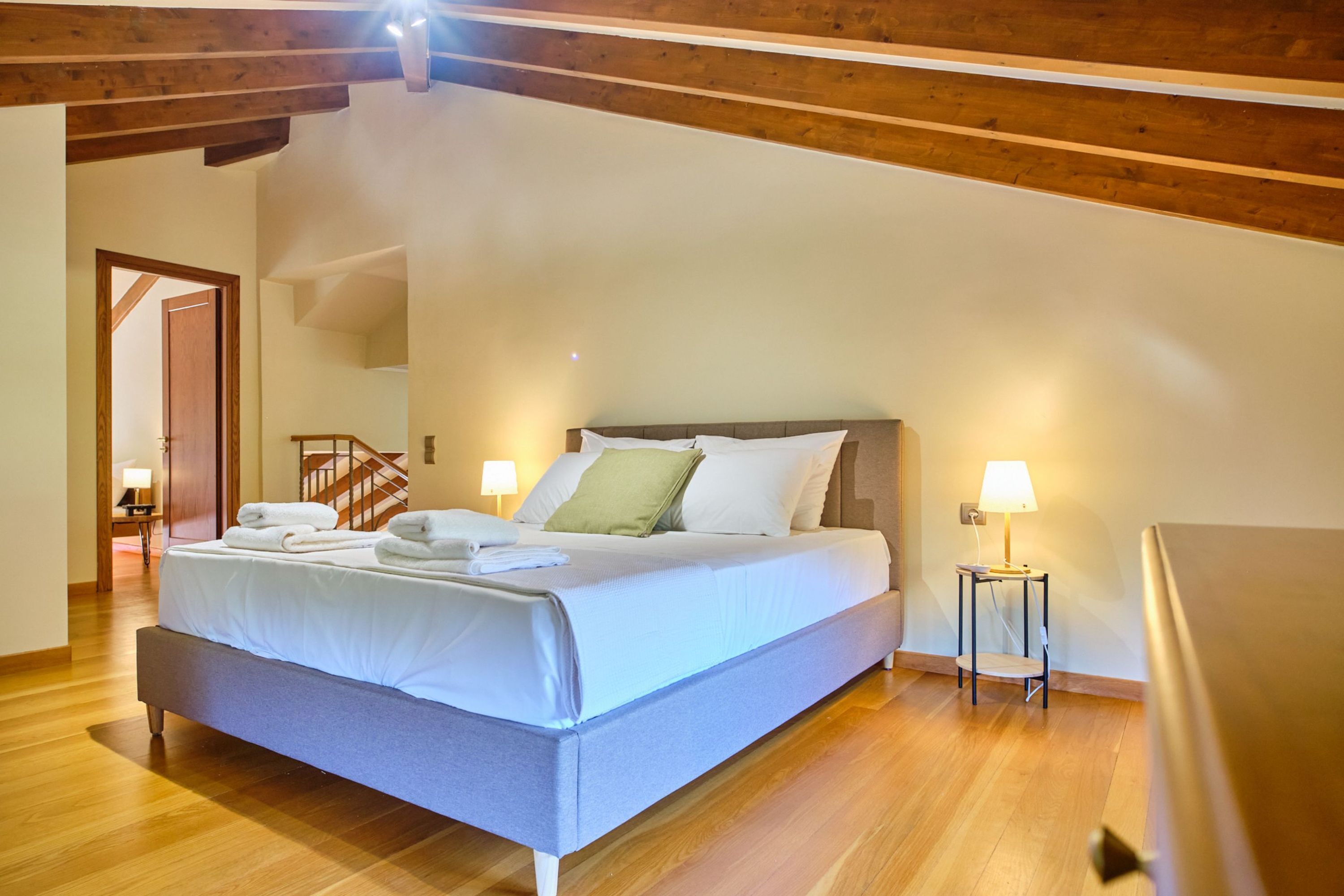 Un dormitorio con cama, suelo de madera y una escalera que lleva a otra habitación.