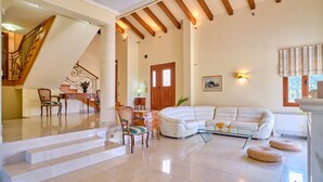 Ein geräumiges Wohnzimmer mit einem weißen Modulsofa, einem Glastisch und einer Treppe, die zu einer anderen Ebene führt.