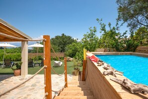 A wooden deck leading to a swimming pool with lounge chairs and umbrellas in the background. - Villa Villekulla in Ionian Islands (Corfu)