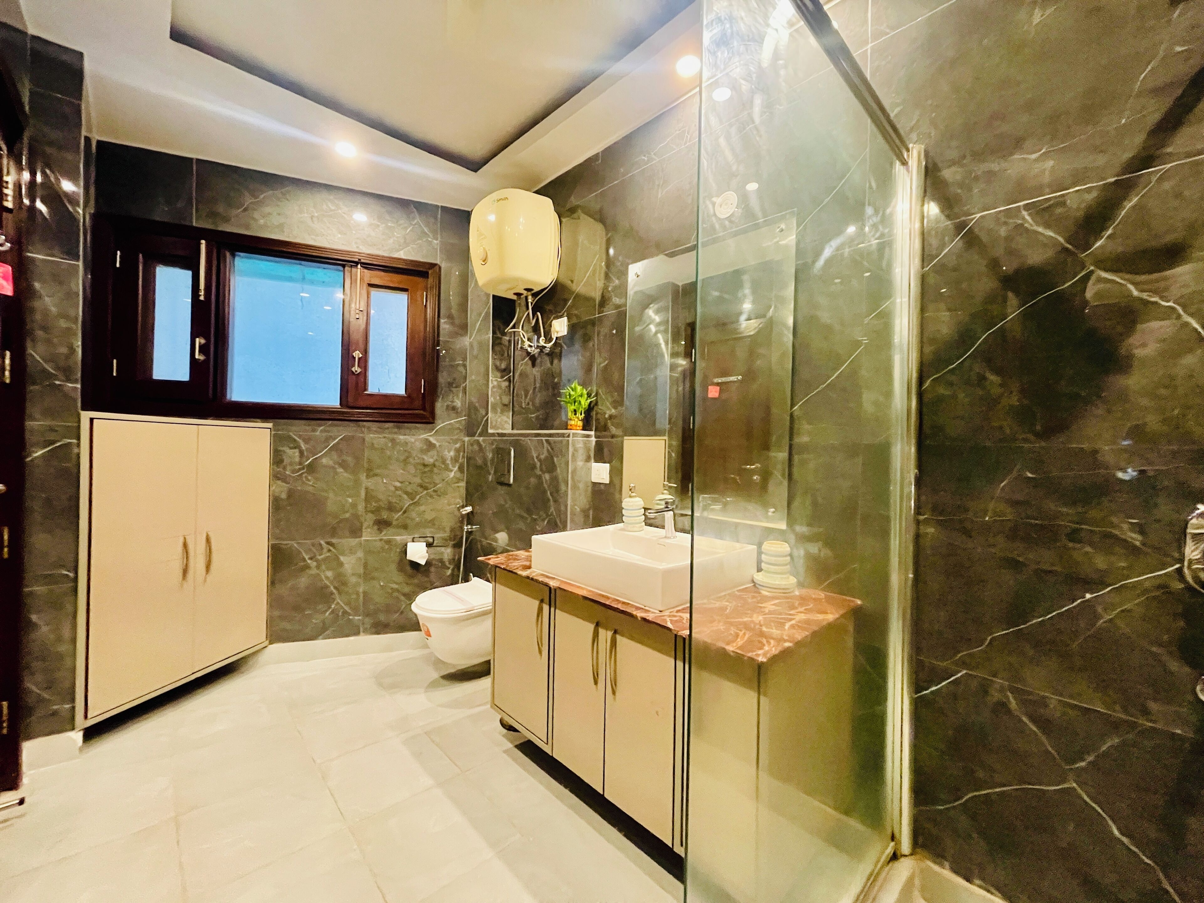 A modern bathroom with a marble floor, a glass shower enclosure, a toilet, and a sink with a marble countertop.